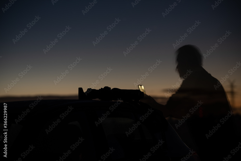 Silhouette of a person on a car in dark night with  cameras utensils on the roof