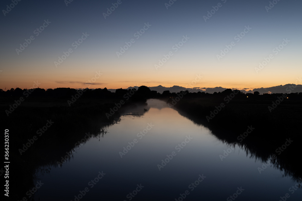 a river glows at night with the horizon along with dark landscape