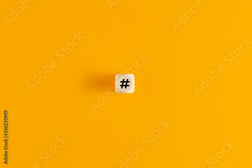Hashtag symbol on wooden cube against yellow background. Overhead view with copy space.