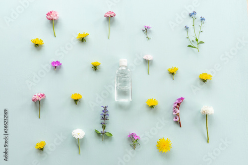 Floral pattern on blue, summer concept. Leaves and little meadow flowers. Clear bottle with lotion in the center.