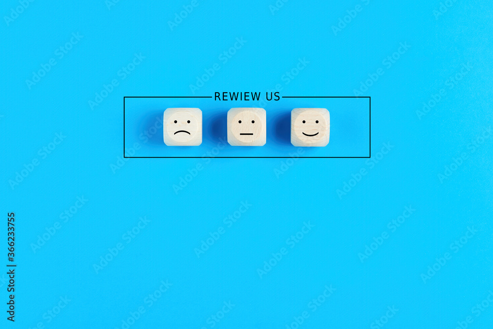 The word review us with happy sad and neutral emoticon faces on wooden cubes. Customer satisfaction, evaluation and feedback concept. The word review us with happy sad and neutral emoticon faces on wooden cubes. Customer satisfaction, evaluation and feedback concept.