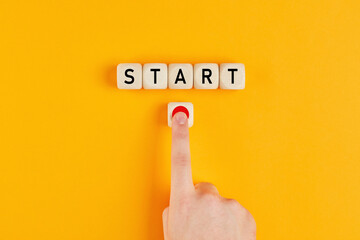 The word start on wooden cubes with a male hand pressing the start button. To make a new start in life, business, education or career concept.