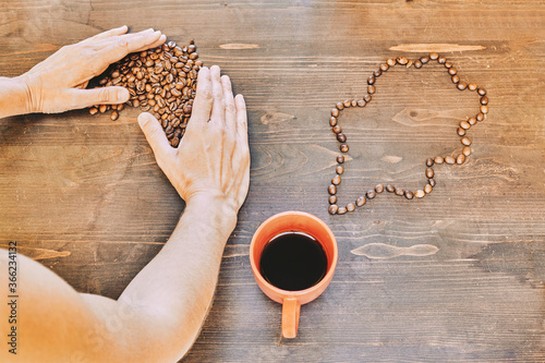 Top view of a person putting roasted coffee beans on a wooden table with a cup of coffee on it