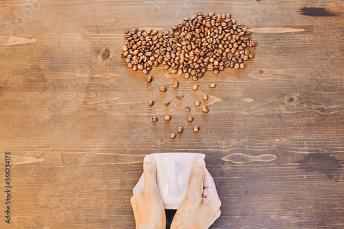 A top view of a person holding a white cup with roasted coffee beans on the table