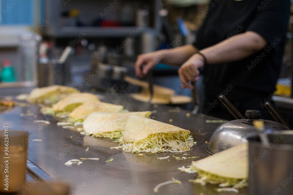 Hand making a Japanese Hiroshima style layered pancake, Okonomiyaki, on a hot pan.