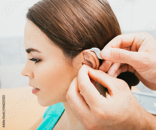 Audiologist inserting hearing aid on female ear, close-up . Deafness treatment, hearing solution