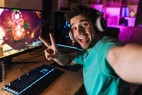 Image of man gesturing peace sign and taking selfie while playing game