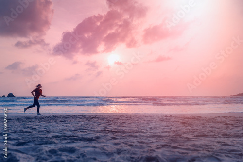 Woman in sports uniform runs along the ocean shore at dawn sunset, jogging and active healthy lifestyle