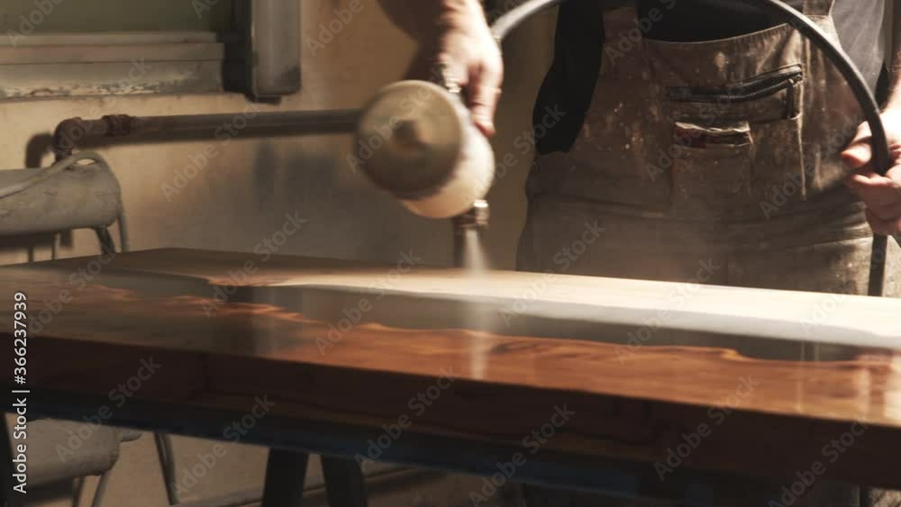Close-up of a male carpenter's hands spraying varnish or primer using compressed air on a wooden tabletop. Furniture manufacture.