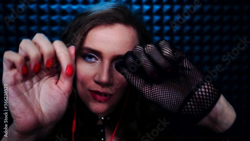 Young smiling woman is doing ASMR sounds - relaxing gloves and hand sound. Black glove is the best trigger for deep relax. Hands touching the face of viewer, massage. Close whispering from ear to ear photo