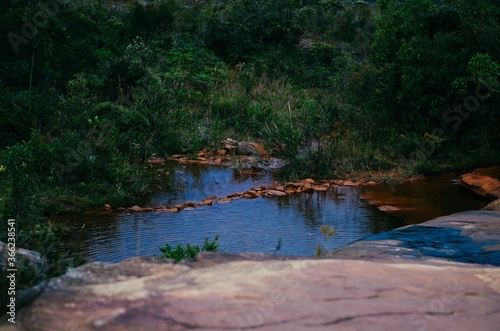 Top view of a calm water cascade in Cachoeira das Andorinhas in Ouro Preto surrounded by greenery and red rocks.