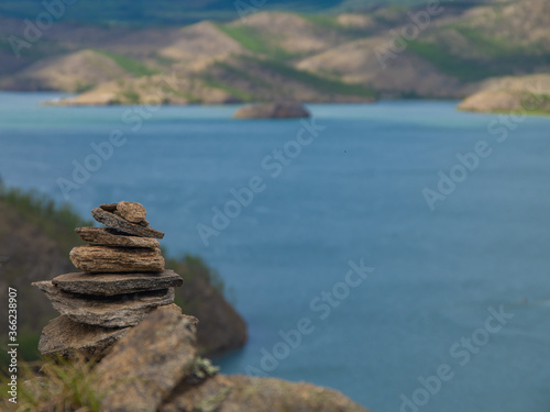 The balanced stone pyramid was made by tourists on the shore of the open water of a mountain lake. Zen stones in balance by the lake