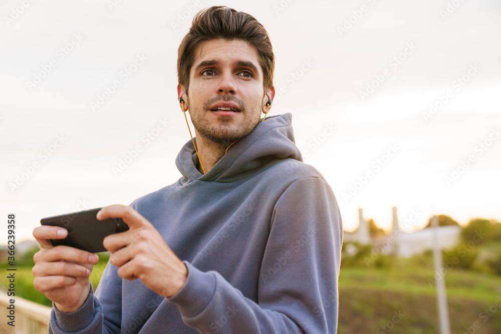 Image of young sportsman with earphones playing video game on cellphone Image of young sportsman with earphones playing video game on cellphone