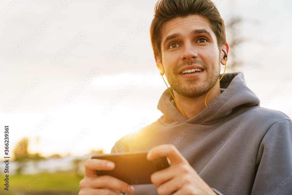 Image of young sportsman with earphones playing video game on cellphone Image of young sportsman with earphones playing video game on cellphone