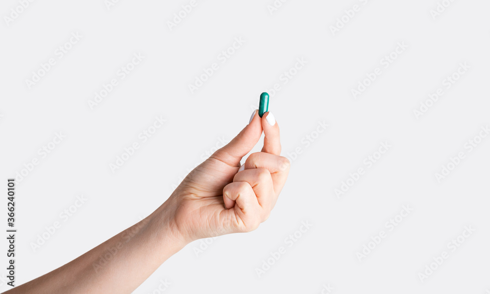 Unrecognizable young girl showing one blue pill over white background, closeup