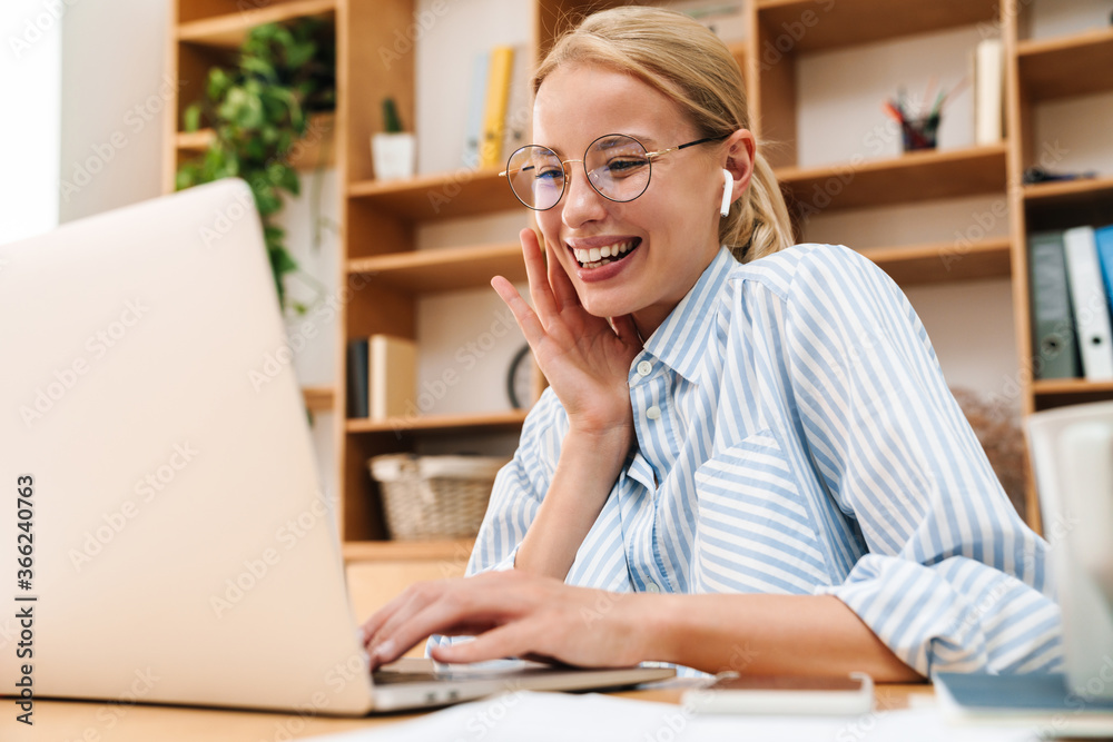 Image of woman using earphones and laughing while working with laptop Image of woman using earphones and laughing while working with laptop