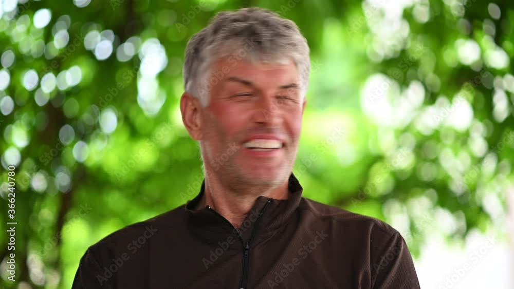 Happy smiling man with grey hair talking in the garden with green background Happy smiling man with grey hair talking in the garden with green background