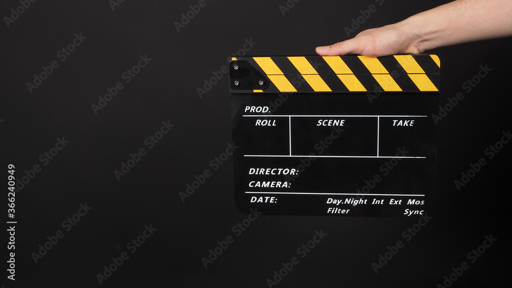 Hand is holding yellow and black color movie slate.It is used in video production and film industry on black background.