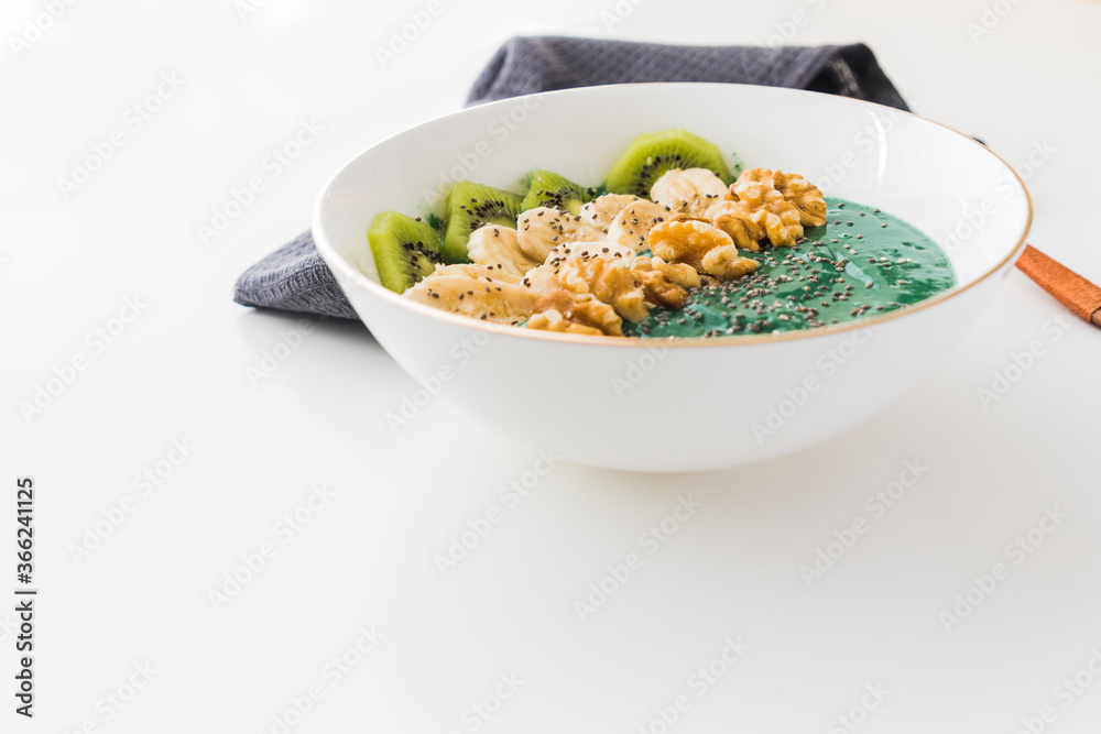 spirulina smoothie bowl with banana, walnuts, kiwi and chia seeds on white background spirulina smoothie bowl with banana, walnuts, kiwi and chia seeds on white background