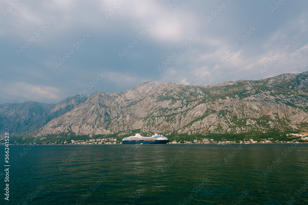 A huge multi-deck cruise liner in Kotor Bay, against the backdrop of a mountain above the city of Dovrota and Ljuta in Montenegro.