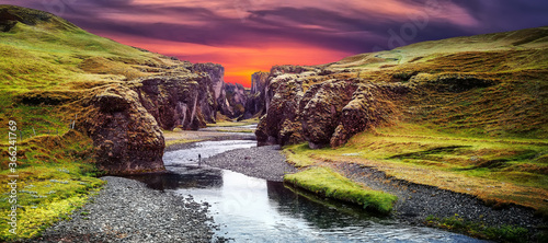 Fantastic view on picturesque canyon Fjadrargljufur with green grass and icelandic moss near river with waterfall. Tipical Icelandic scenery during sunset. Amazing nature landscape during sunset