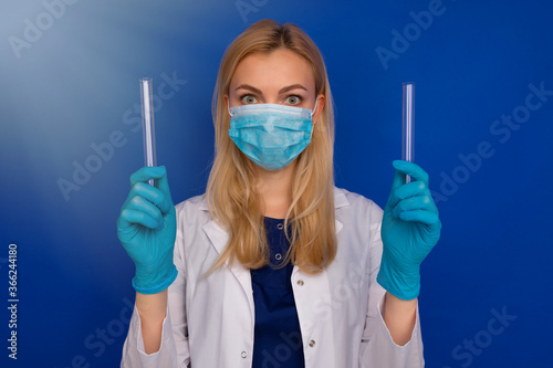A girl doctor in a medical mask and gloves holding test tubes on a blue background