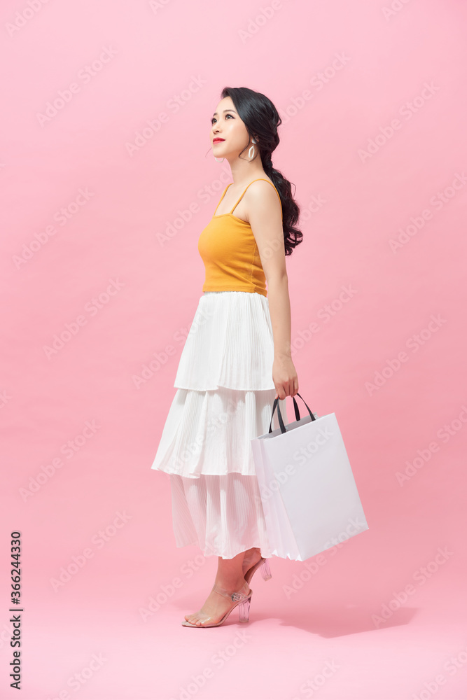 Full length of young woman holding shopping bags and smiling while walking isolated over pink background. Full length of young woman holding shopping bags and smiling while walking isolated over pink background.