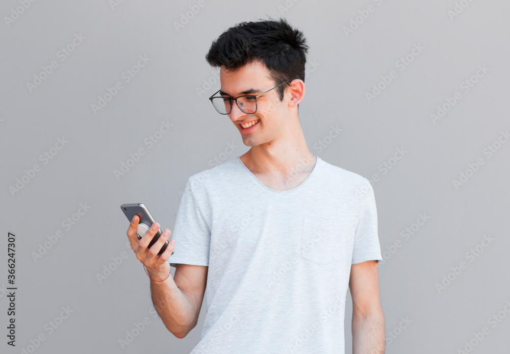 Smiling young man looking at his smart phone while text messaging isolated on grey background