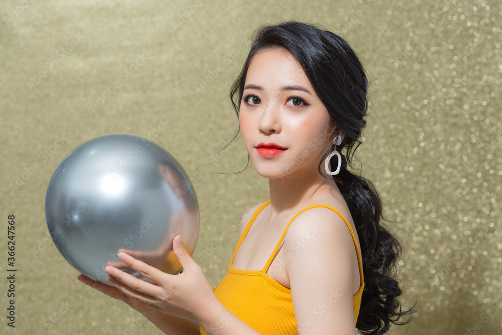 Naklejka premium Beautiful young Asian woman holding ballon when standing isolated over gold background.