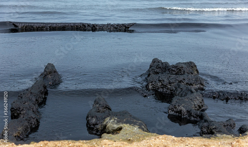 The sea and the beach are polluted with oil. A crude oil spill on the sand of a city beach. Beach oil spill impact, pollution, waste disposal. Ecological catastrophy