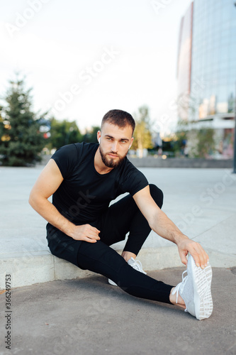 Athletic runner, sport man doing stretching exercise preparing for morning workout outdoors in city. Young man sports exercises. Runner stretches legs muscles making functional training space for text © Dima