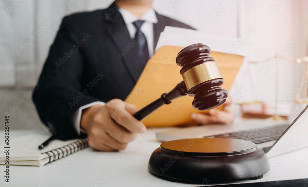 Justice and law concept.Male judge in a courtroom with the gavel, working with, computer and docking keyboard, eyeglasses, on table in morning light