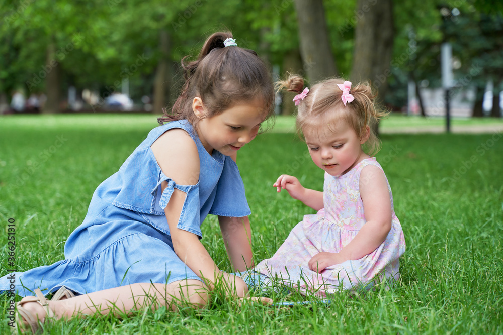 a big girl and a little girl are sitting on the green grass looking at the phone a big girl and a little girl are sitting on the green grass looking at the phone