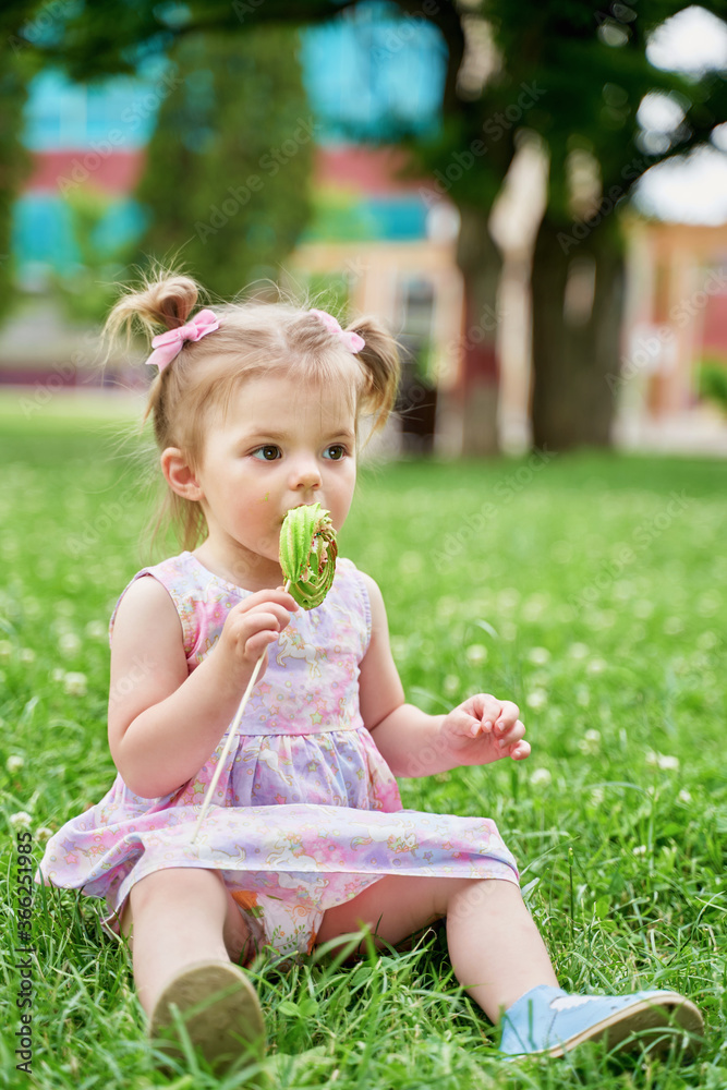 a little girl in a pink dress eats a green candy a little girl in a pink dress eats a green candy