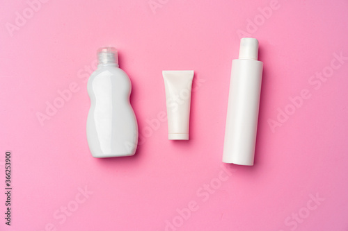 Three white cosmetic bottles on pink background flat lay