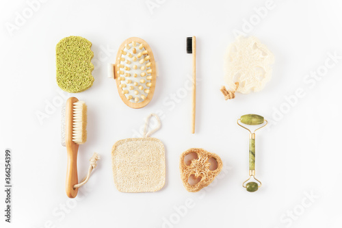 Eco friendly items on white surface. Bamboo toothbrush, detangling hair brush, exfoliating loofah sponge, massaging brush, quartz face roller. Sustainable lifestyle. Skin care concept