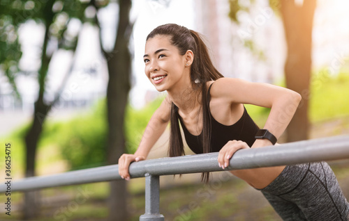 Outdoor Training. Sporty asian girl doing push ups with handrail as mainstay