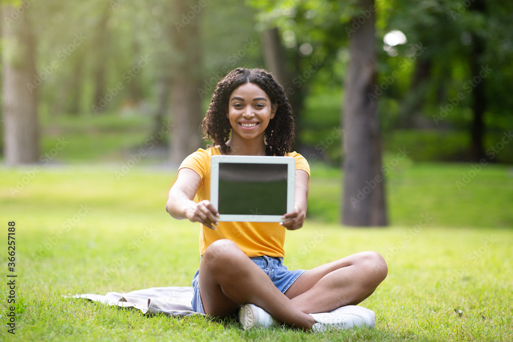Happy African American girl showing tablet computer with empty screen at park, space for design