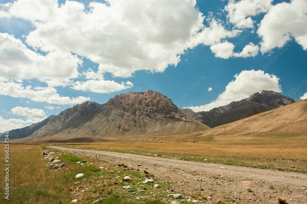 Dirt road in mountains. White clouds blue sky of Central Asia, at the height of 4,000 meters