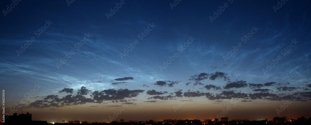 Beautiful panorama of the night city with silver mesospheric clouds. Late twilight. Shining in the sky. The sun over the horizon in the early morning. Noctilucent clouds.