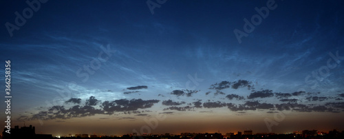 Beautiful panorama of the night city with silver mesospheric clouds. Late twilight. Shining in the sky. The sun over the horizon in the early morning. Noctilucent clouds.