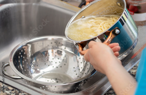 Fotografie woman separating water from spaghetti withempty silver colander