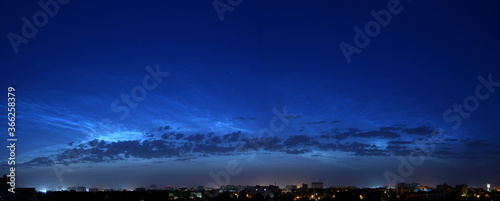 Panorama of a beautiful blue predawn sky with silvery mesospheric clouds. Noctilucent clouds. Late twilight. Night city. The sun is beyond the horizon.