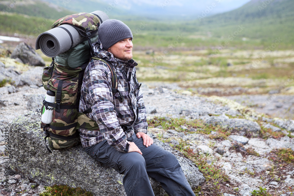 Backpacker enjoying while resting on stone in mountain valley, tired man with backpack is in mountains, copyspace Backpacker enjoying while resting on stone in mountain valley, tired man with backpack is in mountains, copyspace