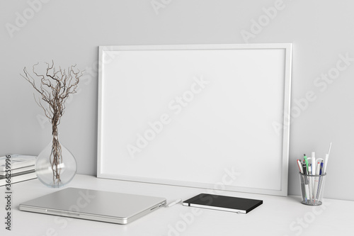 Horizontal poster frame mockup on the white table of home studio workspace with white wall. Side view, clipping path around poster picture.
