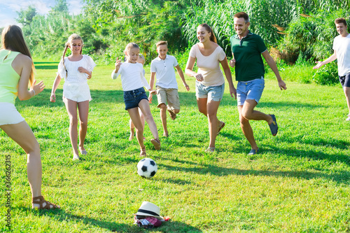 Two happy italian friendly families with children playing football in nature at summer