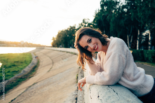 a girl in a light pink sweater smiles at the sunset on the embankment © Татьяна Палладина