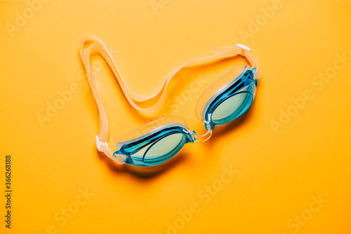 Blue swimming glasses, with rubber strap on yellow background.