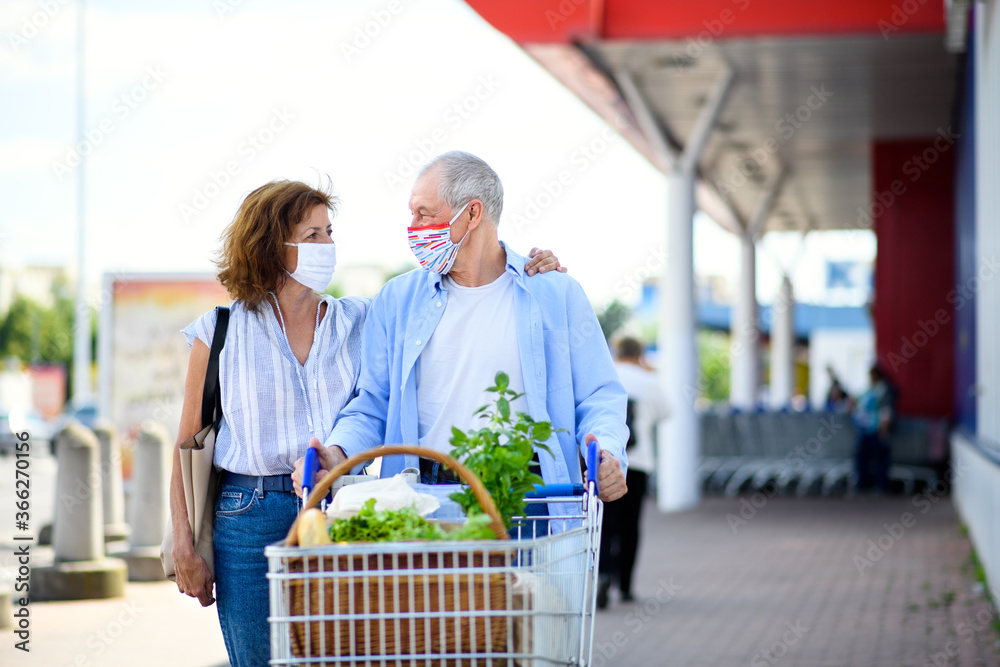 Senior couple with face masks and shopping walking outside supermarket in city. - obrazy, fototapety, plakaty 