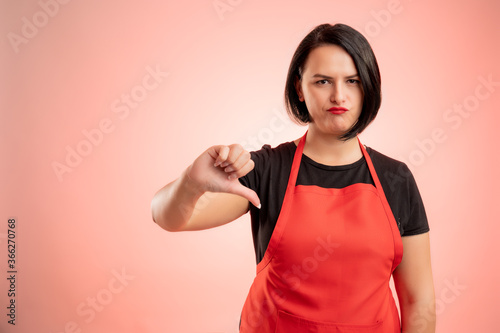 Woman employed at supermarket with red apron and black t-shirt showing dislike